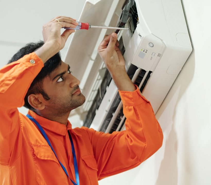 Indian man setting up air conditioner Concentrated young Indian engineer in orange wear using screwdriver while setting up air conditioner